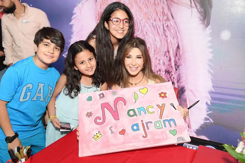 Nancy Ajram posing with young fans who hold a pink sign